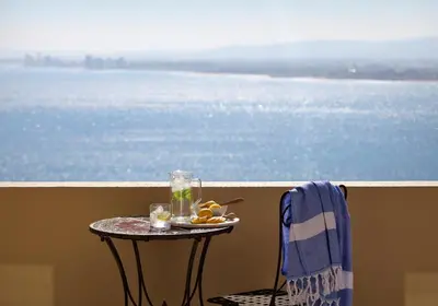 a table with a plate of food on a balcony with the water at Bayview in Gordonʼs Bay