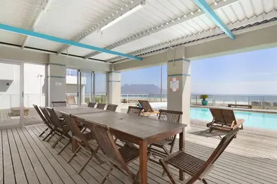 a dining room with a table and chairs and a pool at Sea Spray AG04 in Bloubergstrand