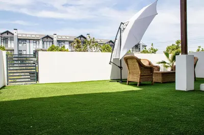 a patio with an umbrella and chairs on the grass at B&B Sitari County Estate - The Most Iconic Estate in Cape Town