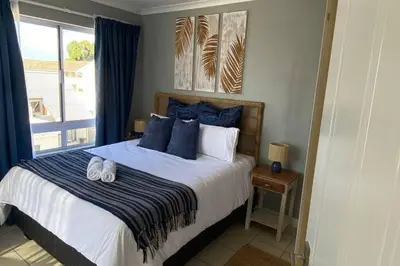 a bedroom with a bed with blue pillows and a window at Ocean Escape in Strand