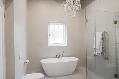 a white bathroom with a tub and a chandelier at Laborie Jonkershuis in Paarl