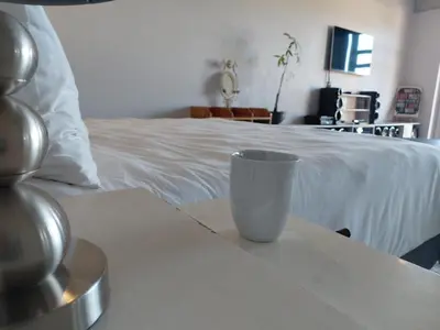 a white cup sitting on a table next to a bed at Chapman View Studio in Cape Town