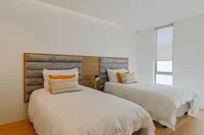a bedroom with two beds with white sheets and orange pillows at 91 Atlantic Drive in Hermanus
