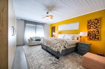 a bedroom with yellow walls and a bed and a chair at Florie se Huis in Paarl