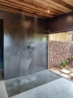 a glass shower in a bathroom with a stone wall at Steenbok farm cottages Sunbird Cottage in Wolseley