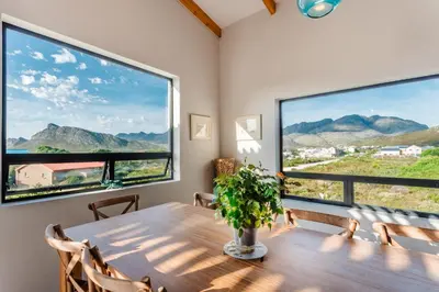 a dining room with a table and two large windows at Prinia on Peak in Pringle Bay in Pringle Bay