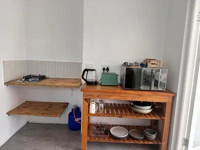 a kitchen with a microwave and a shelf with dishes at Sunset Studio Garden View in Cape Town