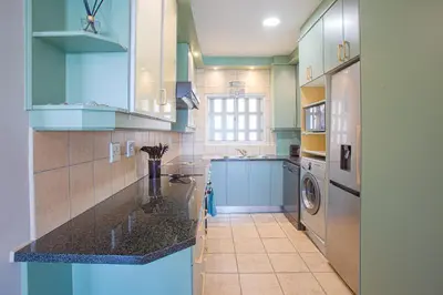 a kitchen with blue cabinets and a washer and dryer at Isla's Place (Strandsig 304) in Cape Town