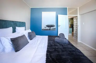 a bedroom with a white bed with a blue wall at Isla's Place (Strandsig 304) in Cape Town