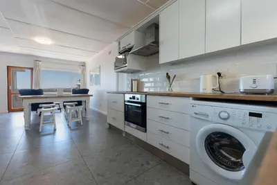 a kitchen with a washing machine and a table with chairs at 'Seaside Cottage', Sleeps 4 with a 3 minute walk from the beach! in Cape Town