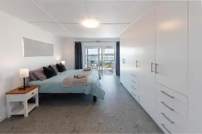a white bedroom with a bed and a window at 'Seaside Cottage', Sleeps 4 with a 3 minute walk from the beach! in Cape Town