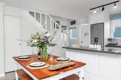 a white kitchen with a wooden table with a vase of flowers at Cosy Home in Claremont in Cape Town