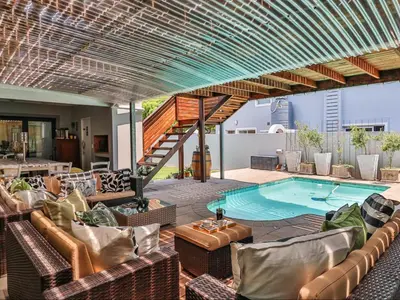 a patio with a swimming pool with chairs and a table at Hermanus Cliff Path Lodge - No Load-shedding in Hermanus