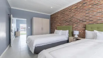 a bedroom with two beds and a brick wall at Inkantu Apartments & Suites in Cape Town