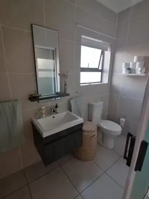 a bathroom with a sink and a toilet and a mirror at The Sandown Blouberg self catering unit in Parklands