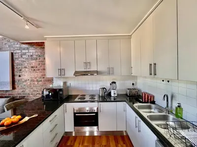 a kitchen with white cabinets and a brick wall at Ben's Apartment in Stellenbosch
