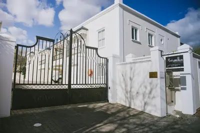 a white house with a black gate and a building at Maison Des Huguenots Le Roux in Franschhoek