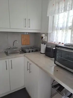 a kitchen with white cabinets and a sink and a microwave at Watercolour Cottage in Hermanus