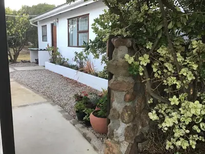 a stone wall in front of a house with flowers at Watercolour Cottage in Hermanus