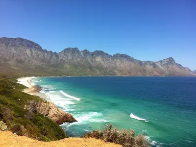a view of a beach with mountains in the background at '79 Protea' Charming self-catering Home, sleeps 6 with Sea Views in Gordonʼs Bay