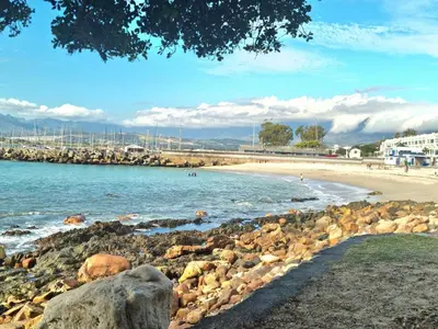 a beach with rocks and people in the water at Beach Apartment on Bikini Beach - sleeps 4 in 2 Ensuite Bedrooms in Cape Town
