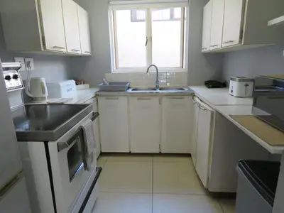 a kitchen with white cabinets and a sink and a window at 'Terrace-On-Sea'- 2 Min from the beach, 2 bedroom town house, Sleeps 4 in Cape Town