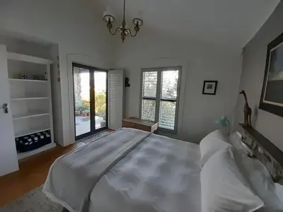 a bedroom with a large white bed and windows at Peaceful Seaside Cottage, Betty's Bay Accommodation in Clareport