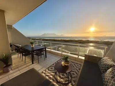 a balcony with a view of the ocean at sunset at Happy Dolphin - Luxury 3BR Sea View Apartment in Cape Town