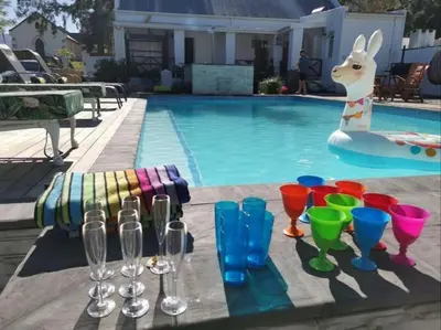 a poolside table with wine glasses and a bunny by a pool at Greyton Toad Hall Historic Private House in Central Greyton in Greyton