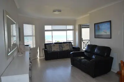 a living room with two black leather couches and windows at Simplicity with an ocean view 200 in Hermanus