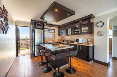 a kitchen with a large island with bar stools at Luxury 3 bedroom Duplex Penthouse with communal swimming pool in Bloubergstrand