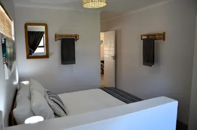 a white bedroom with a bed and a mirror at The Beach Cottage Betty's Bay in Bettyʼs Bay