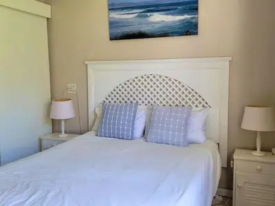 a bedroom with a white bed with blue pillows at Nest Egg Holiday Home Voëlklip in Hermanus