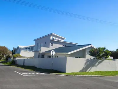 a white house with a white fence next to a street at Nest Egg Holiday Home Voëlklip in Hermanus