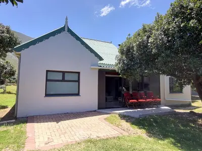 a white house with red chairs in front of it at Milkwood Cottage in Bettyʼs Bay