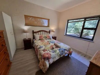 a bedroom with a bed with a floral bedspread and a window at Milkwood Cottage in Bettyʼs Bay