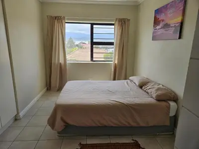 a bedroom with a bed and a large window at Strand Beach Apartment in Cape Town