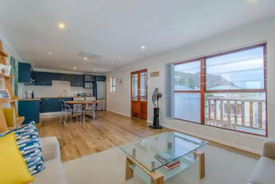 a living room with a glass coffee table and a kitchen at Beachfront Bliss at Malgas Views in Gordonʼs Bay