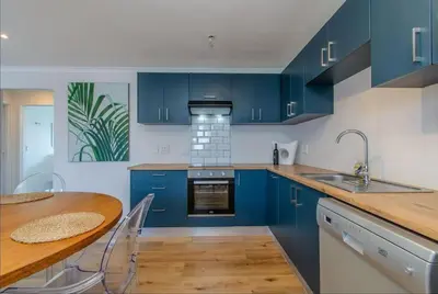 a kitchen with blue cabinets and a wooden table at Beachfront Bliss at Malgas Views in Gordonʼs Bay