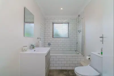 a white bathroom with a tub and a toilet and a sink at Beachfront Bliss at Malgas Views in Gordonʼs Bay