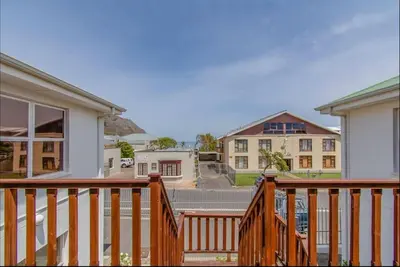 a house with a wooden deck with houses in the background at Beachfront Bliss at Malgas Views in Gordonʼs Bay