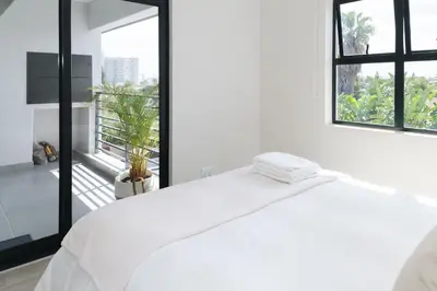 a white bedroom with a bed and a balcony at Blouberg Coastal Hideout, Luxury Apartment with a Braai and Parking in Cape Town
