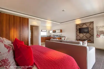 a bedroom with a red bed and a living room at Sunset Beach Luxury Apartments in Cape Town