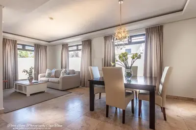 a dining room and living room with a table and chairs at Sunset Beach Luxury Apartments in Cape Town