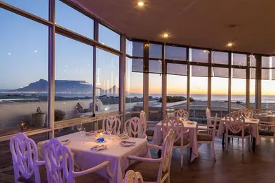 a dining room with tables and chairs and windows at 4-Bedroom cabana at Dolphin Beach in Cape Town