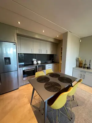 a kitchen with a table and chairs and a refrigerator at Luxury Vineyard Apartment in Cape Town