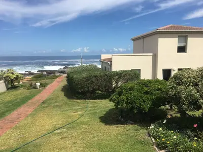 a house with a yard next to the ocean at Oceans Edge - Hermanus Beach Club in Hermanus