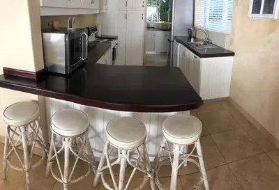 a kitchen with three bar stools and a counter with a microwave at House in Hermanus Voëlklip in Hermanus