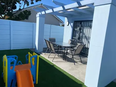a patio with a table and chairs and grass at 32 On Gill Road Self Catering in Cape Town