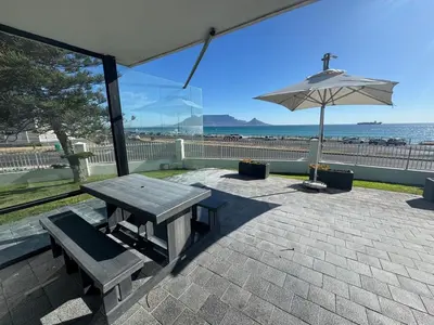 a picnic table and an umbrella in front of the beach at Blouberg Sea View in Bloubergstrand